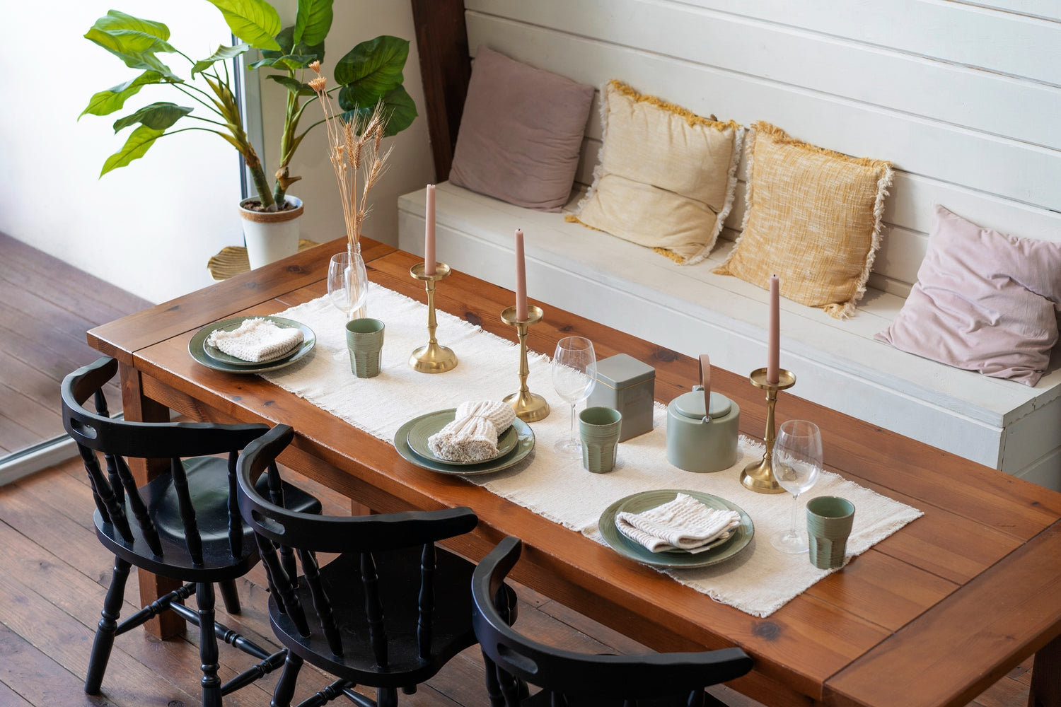 Dining table set with plates, cups, and napkins in a cozy room with a bench and cushions.